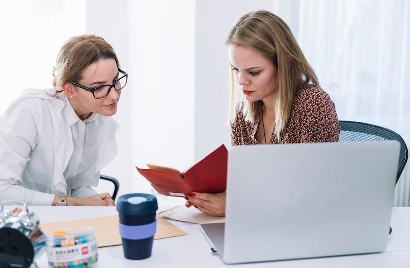 two-female-businesspeople-reading-diary-office_23-2147955052 (1)